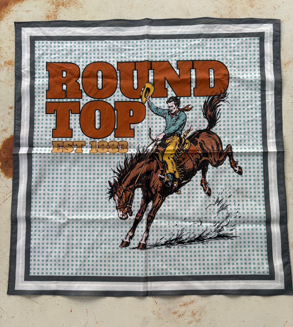 A square bandana featuring a western-themed graphic print with the text 'ROUND TOP EST. 1868' and an illustration of a cowboy riding a bucking brown horse, laid flat on a textured beige surface.
